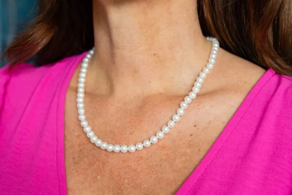 A woman wearing a pink shirt and pearls