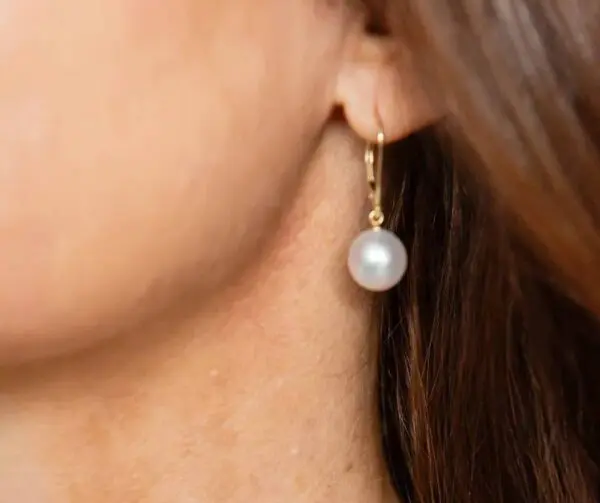 A woman wearing gold earrings with pearls hanging from them.