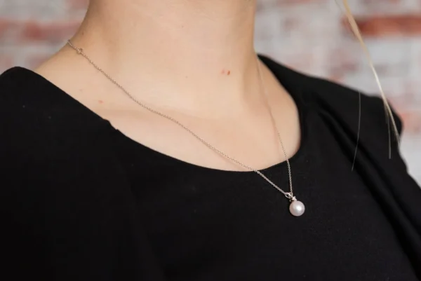 A woman wearing a necklace with a pearl on it.