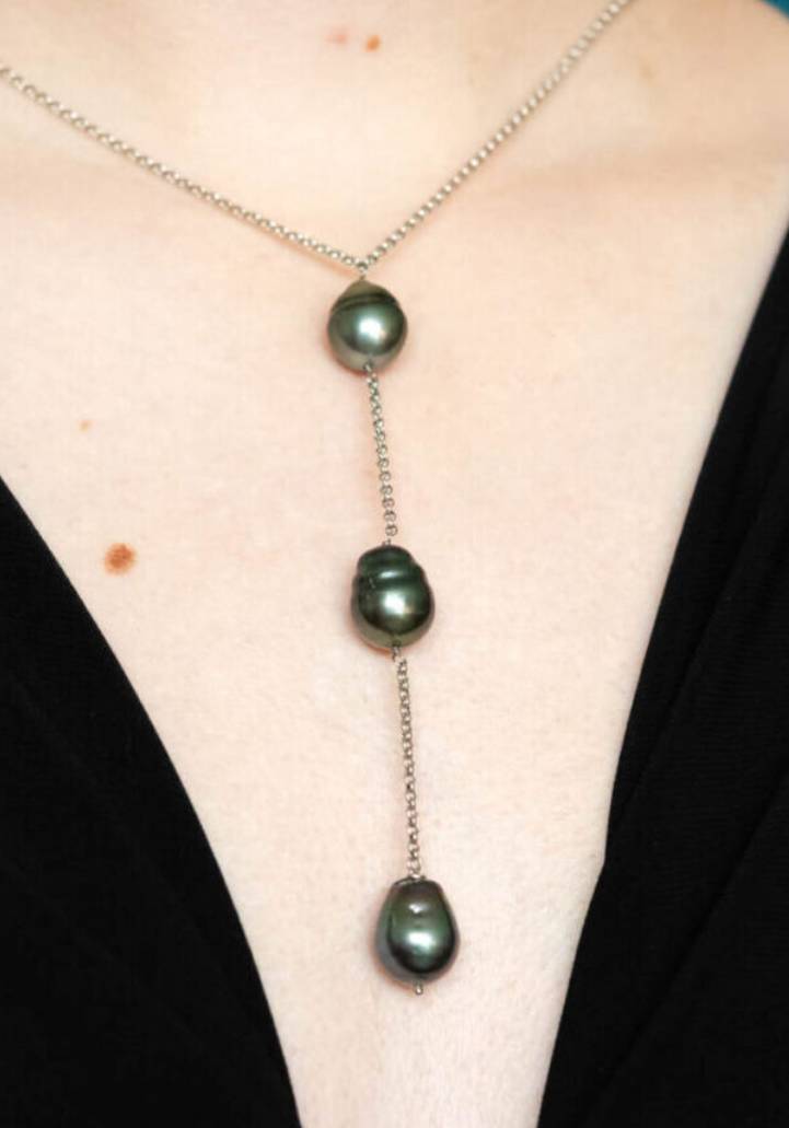 A woman wearing a necklace with three pearls.