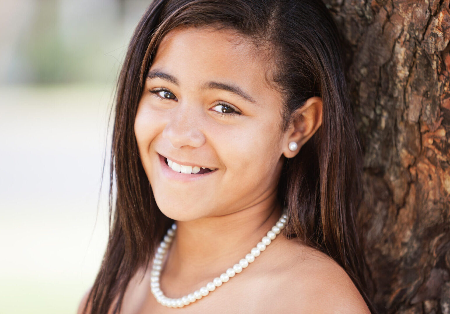 A young girl wearing pearls and smiling for the camera.